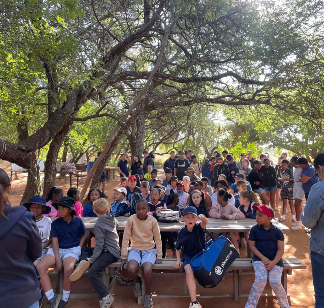 School students gathered under trees for an outdoor leadership talk.