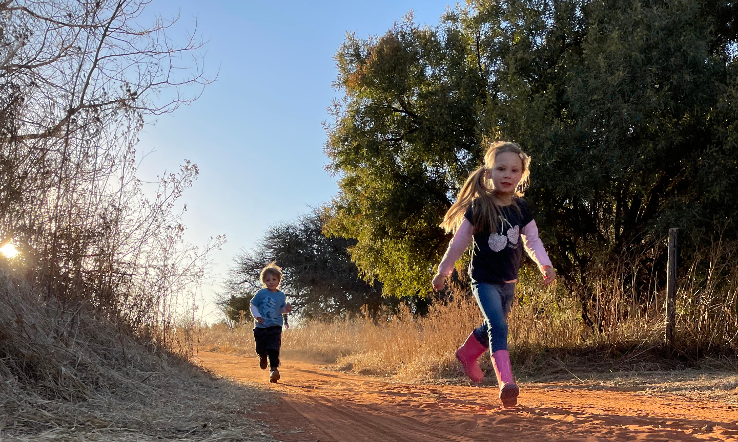 Two children running together on a red sand path at golden hour.