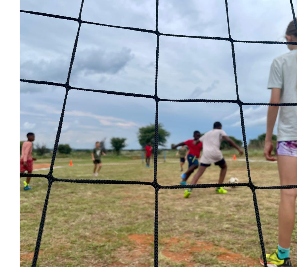 Students playing mini-soccer behind a goal net on the field.