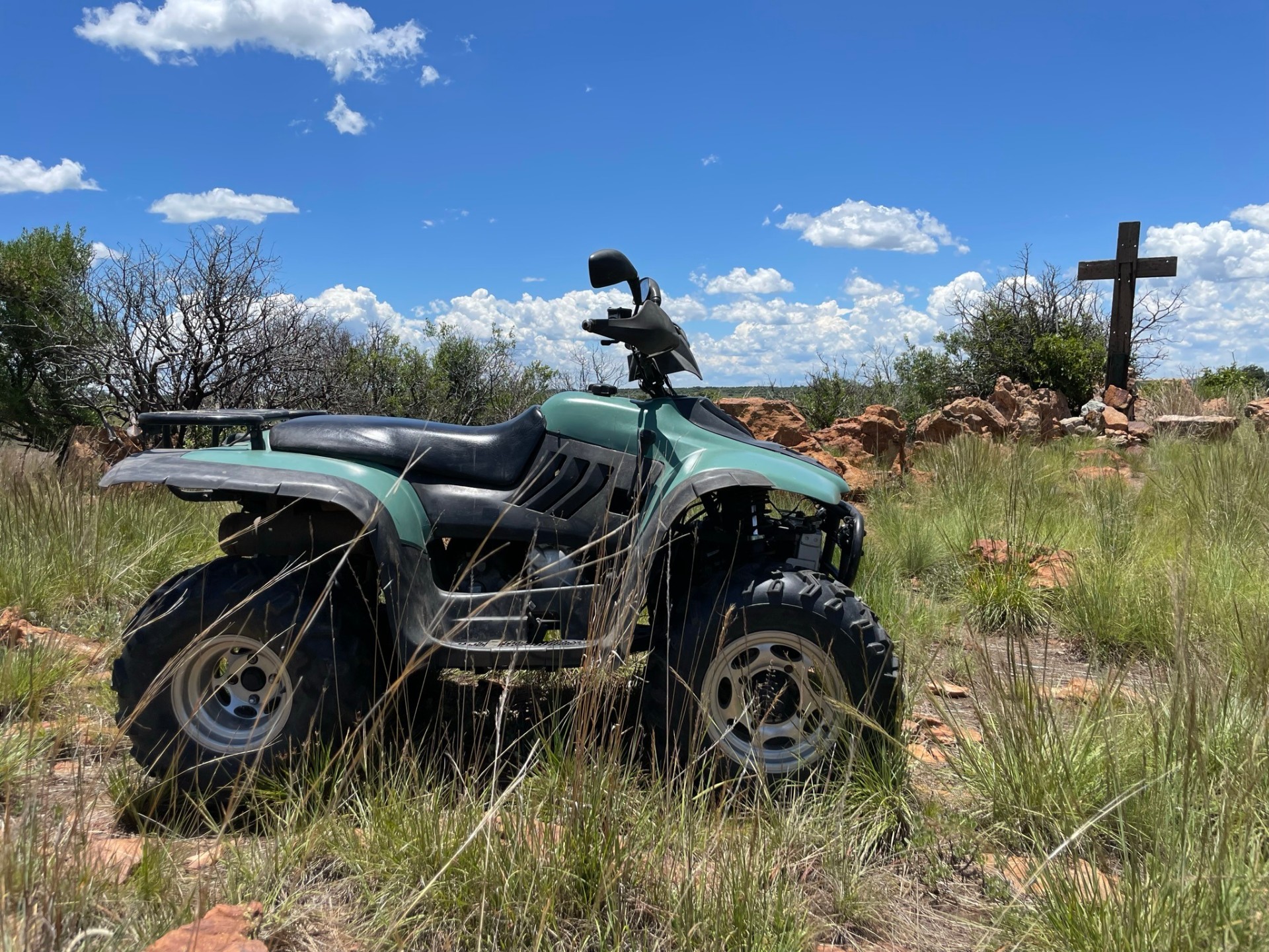 Quad bike parked in the bushveld near a wooden cross.