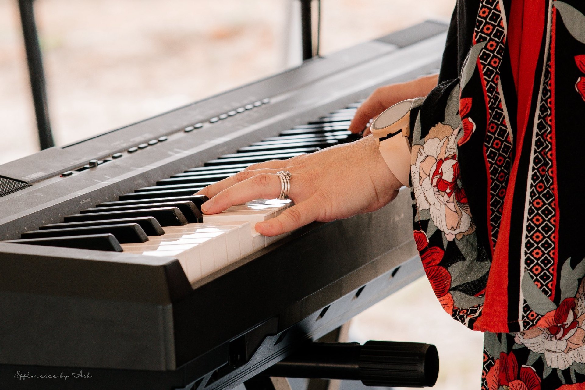 A woman's hand playing piano keys in a sunlit space.